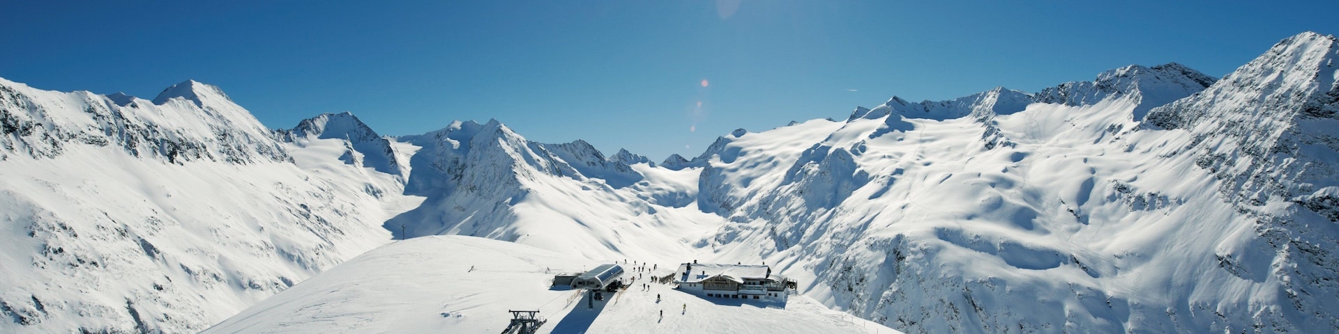 A snowy mountain slope with a ski lift, a lodge, and a clear blue sky.