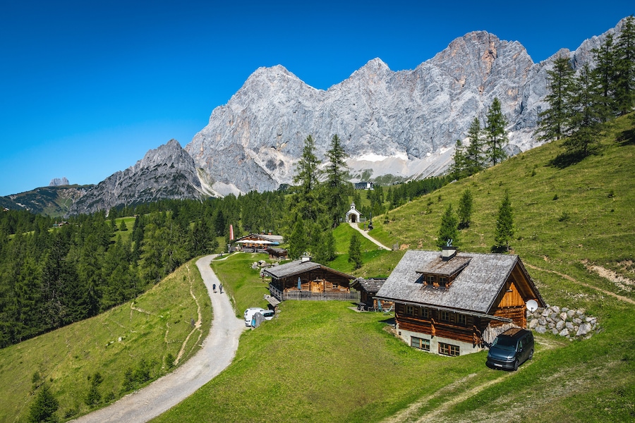 A mountain village with wooden houses, a winding road, and a large mountain in the background.