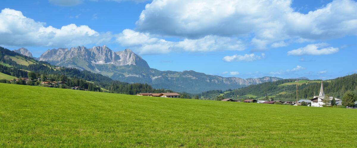 A green field, a church, and mountains in the background.
