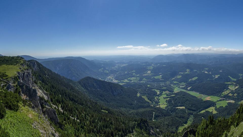 A mountainous landscape with a clear sky, green valleys, and distant mountain peaks.