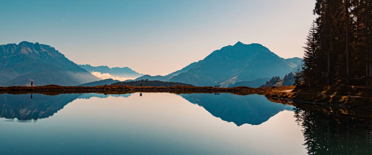 A calm lake reflecting mountains and a person standing on a small island.