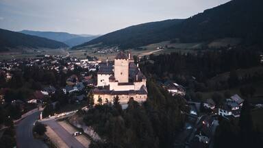 A medieval castle surrounded by a village and forested hills.