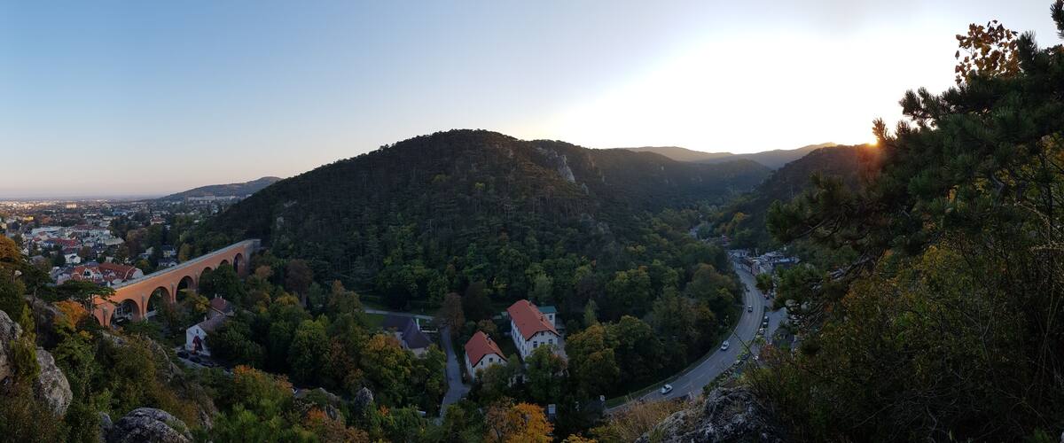 A mountainous landscape with a town nestled in the valley, a winding road, and a bridge.