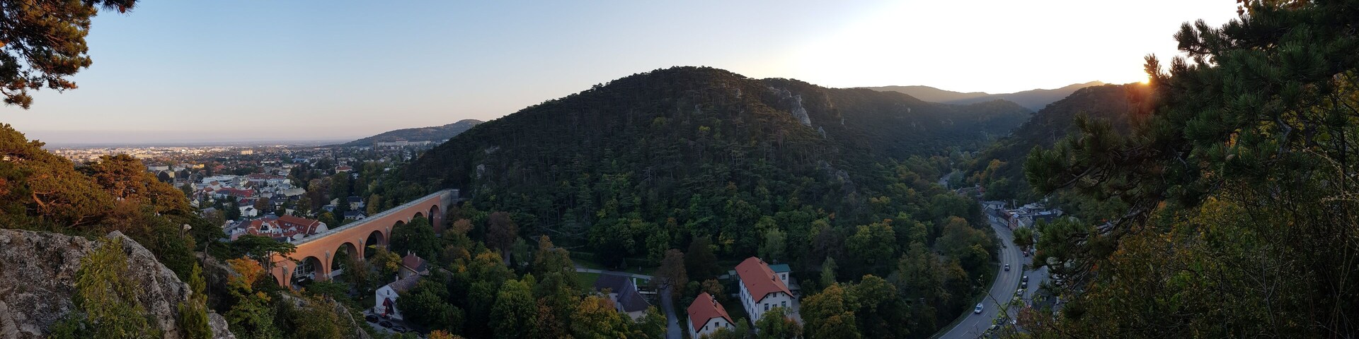 A mountainous landscape with a town nestled in the valley, a winding road, and a bridge.
