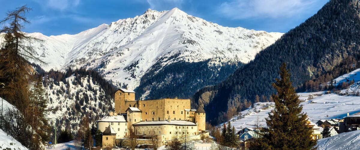 A snow-covered mountain with a castle and houses in the foreground.