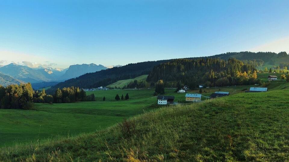 A mountainous landscape with green fields, scattered houses, and dense forests.