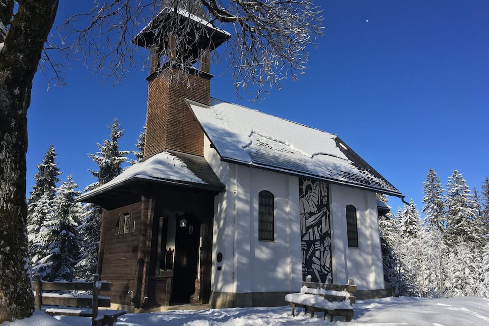 Une église enneigée, dotée d’un clocher et de bancs en bois, se dressant au milieu d’un paysage hivernal.
