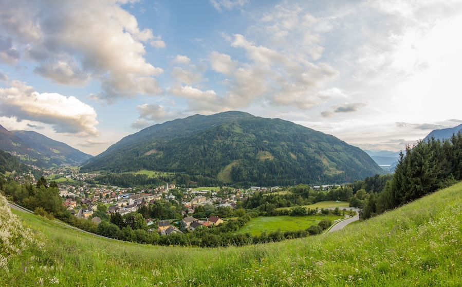 A valley with a town nestled among green hills and a mountain in the background.