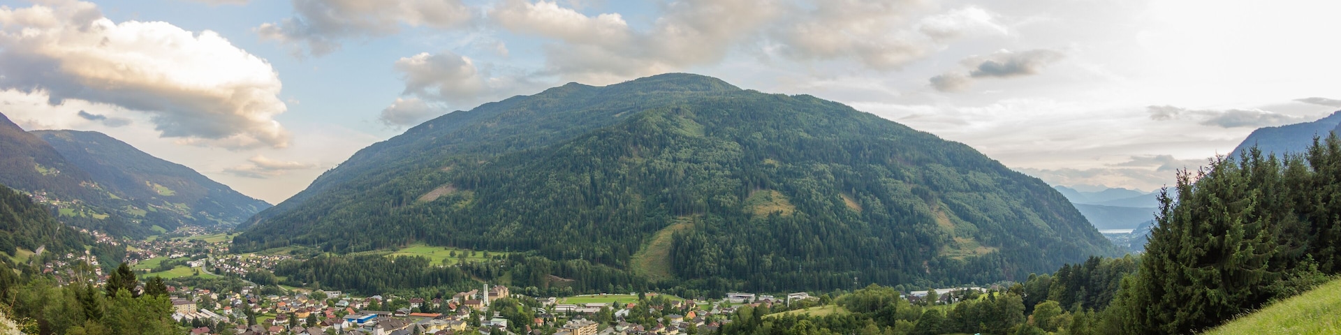 Un valle con un pueblo rodeado de colinas verdes y una montaña al fondo.