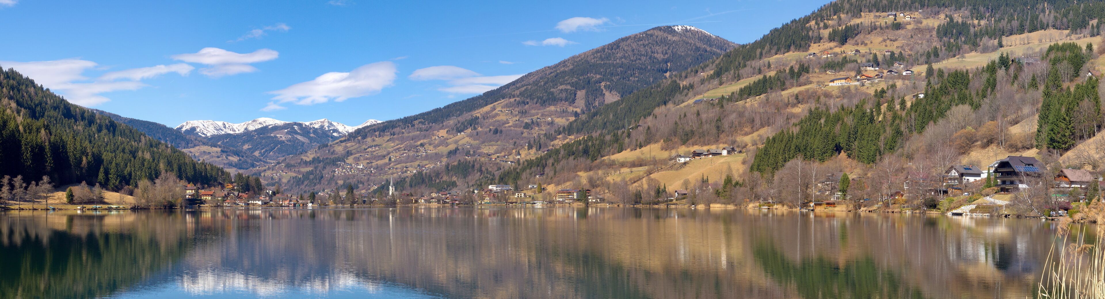 A serene lake surrounded by mountains, a small village, and a church.