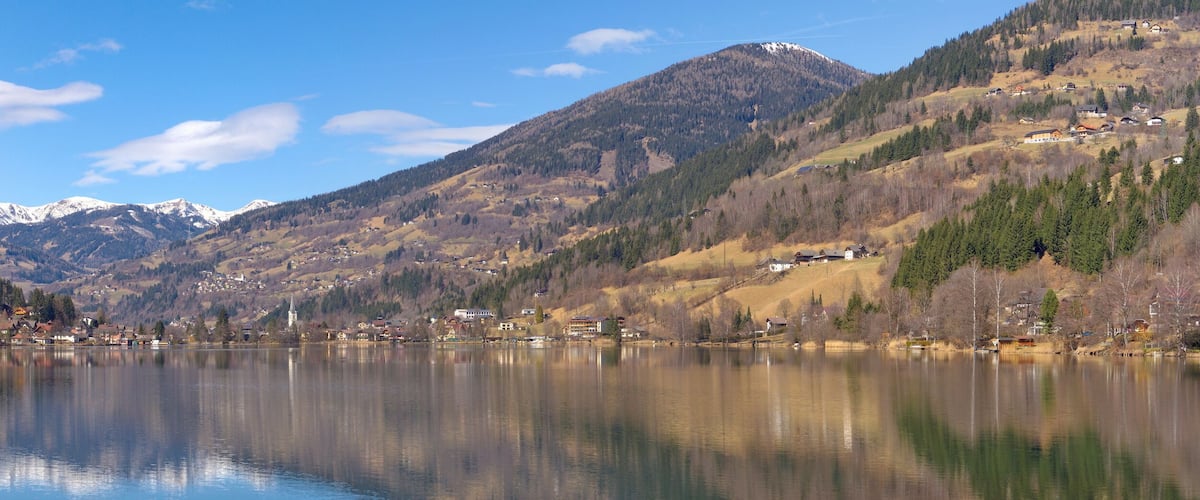 A serene lake surrounded by mountains, a small village, and a church.