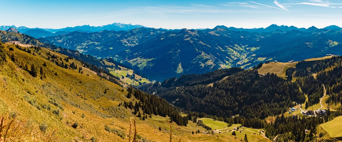 A mountainous landscape with a valley, forested areas, and scattered buildings.