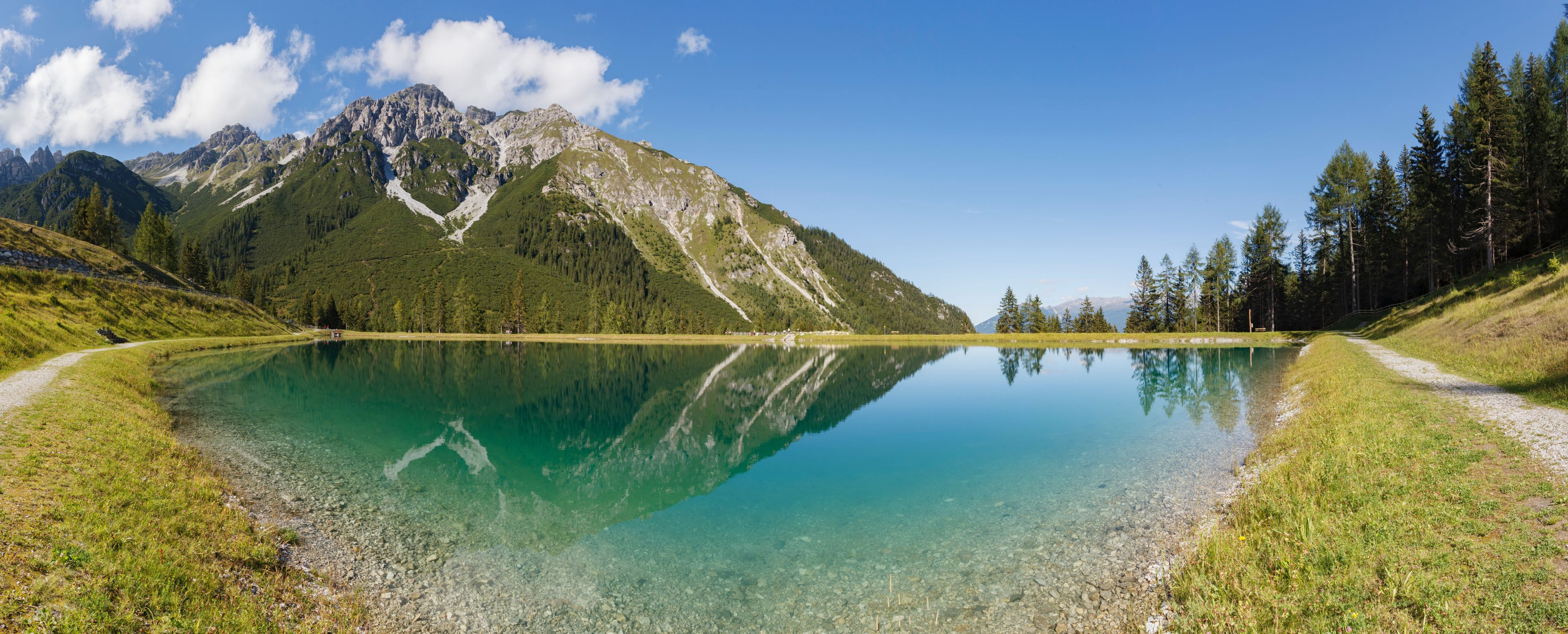 The alpine mountains reflect beautifully in the Panoramasee at Schlick2000 in the Stubai Valley, creating a serene and picturesque scene.