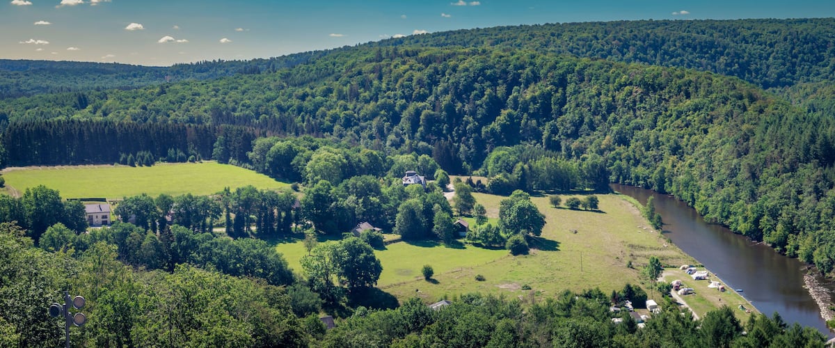 A river winding through a densely forested valley with a small settlement and camping area along the riverbank.