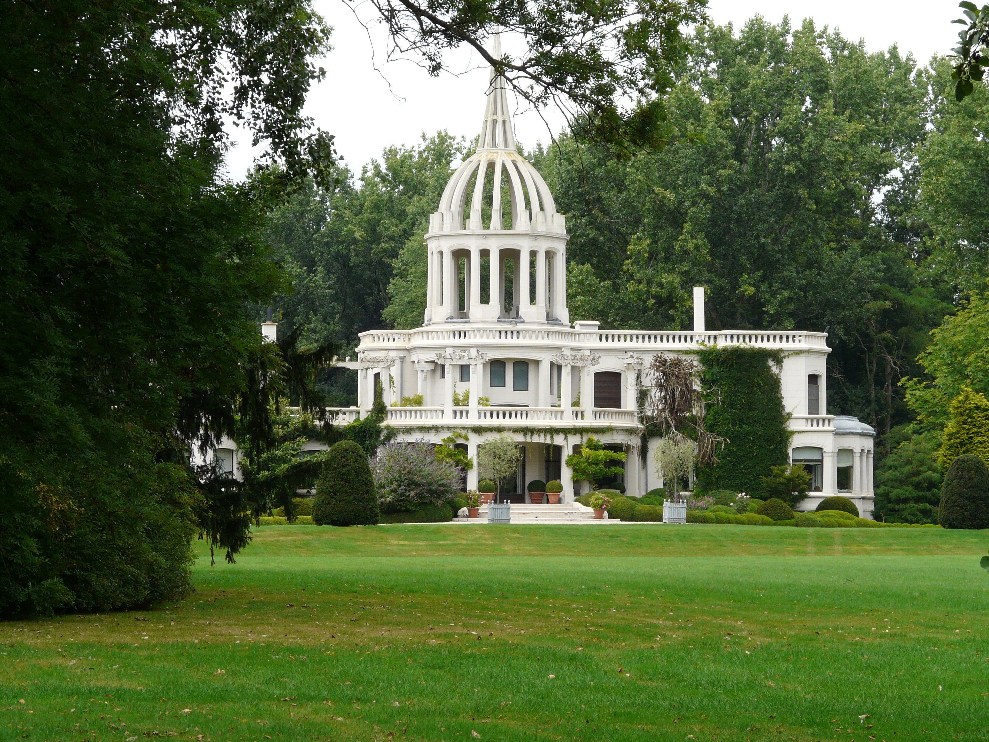 A large white mansion with a central dome and columns, surrounded by lush greenery and a well-maintained lawn.