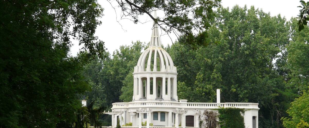 A large white mansion with a central dome and columns, surrounded by lush greenery and a well-maintained lawn.
