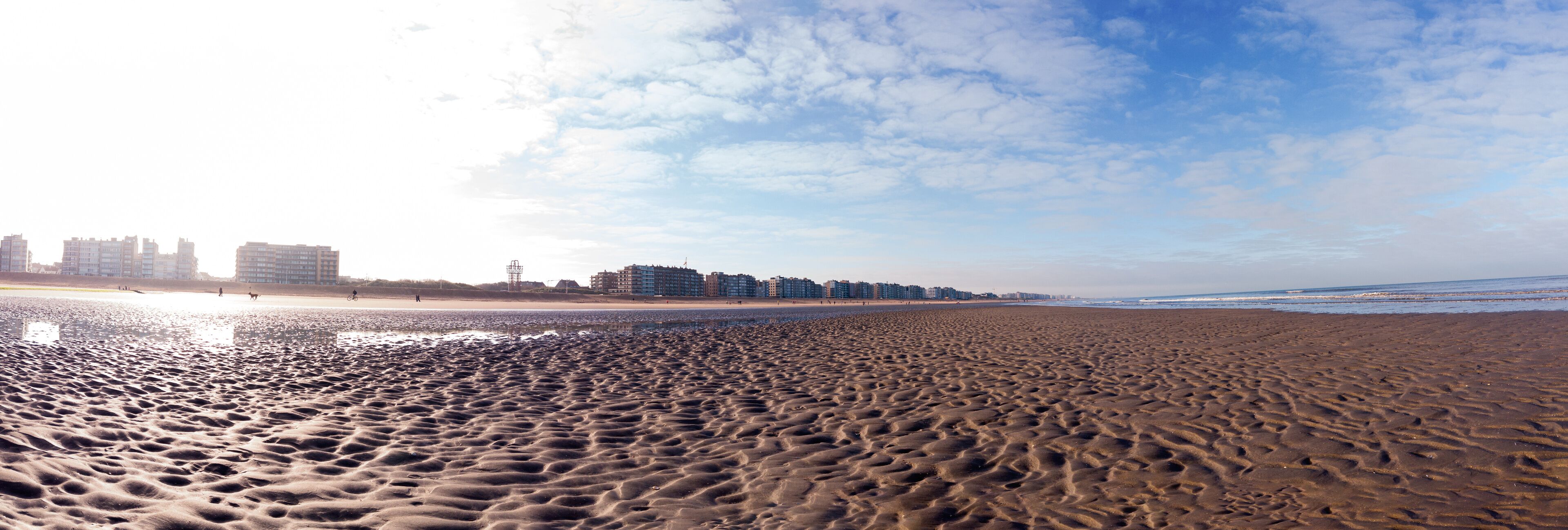 A sandy beach with footprints, a clear sky, and buildings in the background.