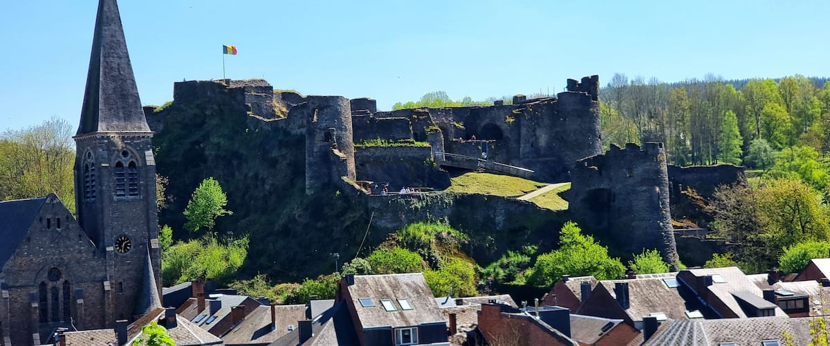 A historic castle atop a cliff with a church and residential buildings below.