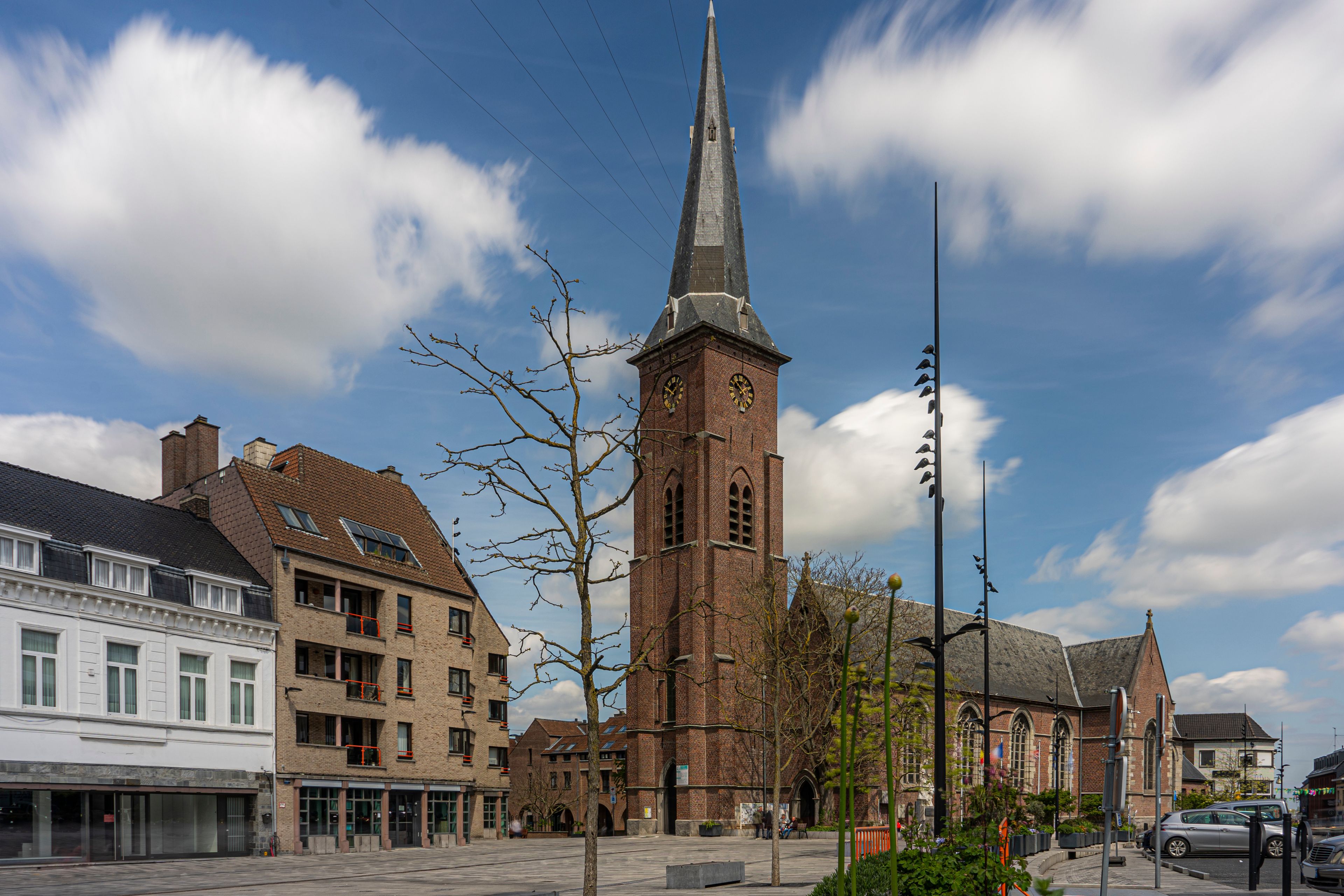 Een kerk met een hoge spits, een rij woongebouwen en een heldere lucht.