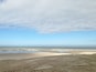 En strand med en sandig förgrund och ett lugnt hav under en delvis molnig himmel.