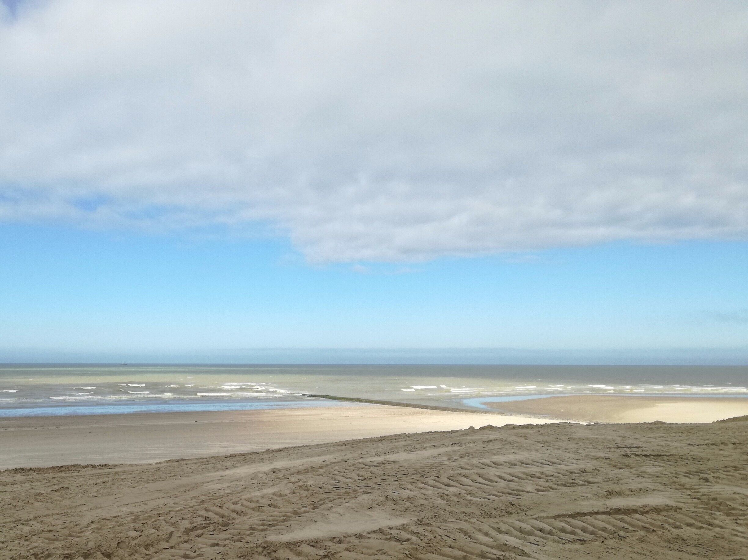 A beach with a sandy foreground and a calm sea under a partly cloudy sky.