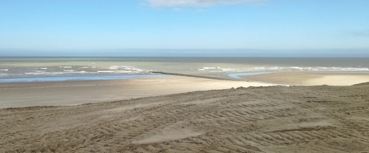 A beach with a sandy foreground and a calm sea under a partly cloudy sky.