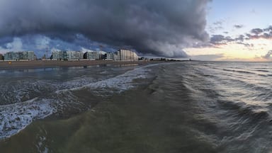 Une plage avec des vagues, un ciel nuageux et des bâtiments en arrière-plan.