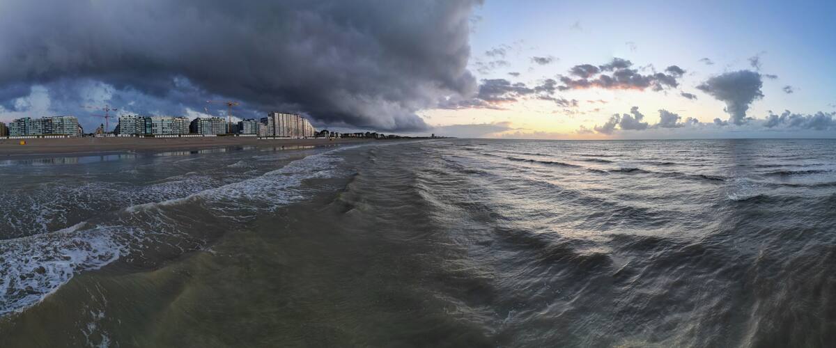 A beach with waves, a cloudy sky, and buildings in the background.