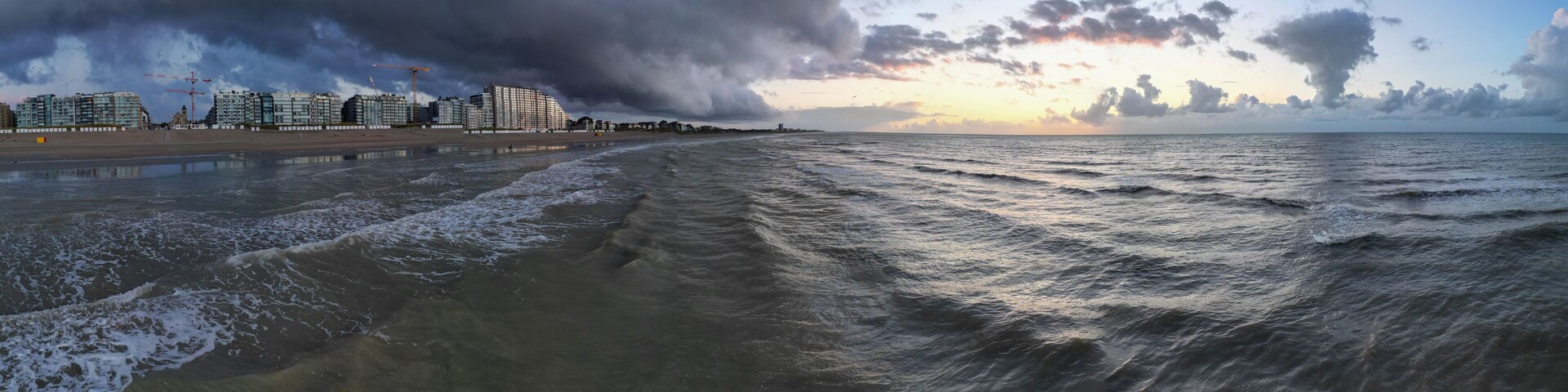 A beach with waves, a cloudy sky, and buildings in the background.