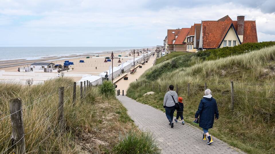 A coastal path leading to a beach with dunes, a wooden fence, and a building with a red roof.