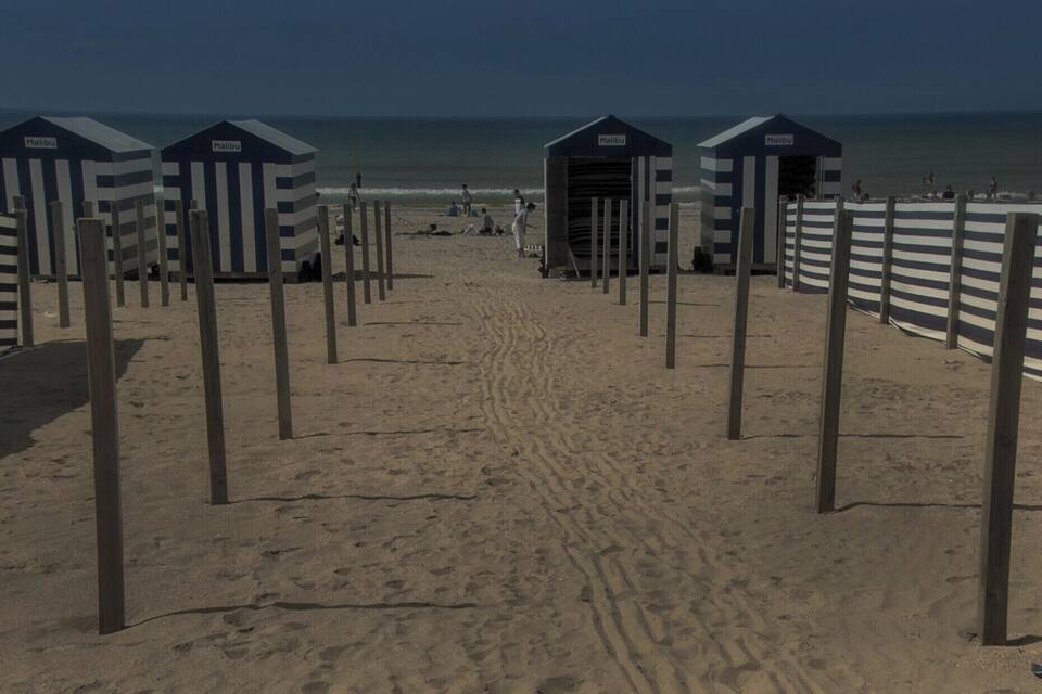 Een strand met gestreepte strandhuisjes en een zandpad dat naar de oceaan leidt.