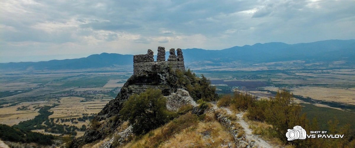 A stone structure on a hill with a valley and mountains in the background.