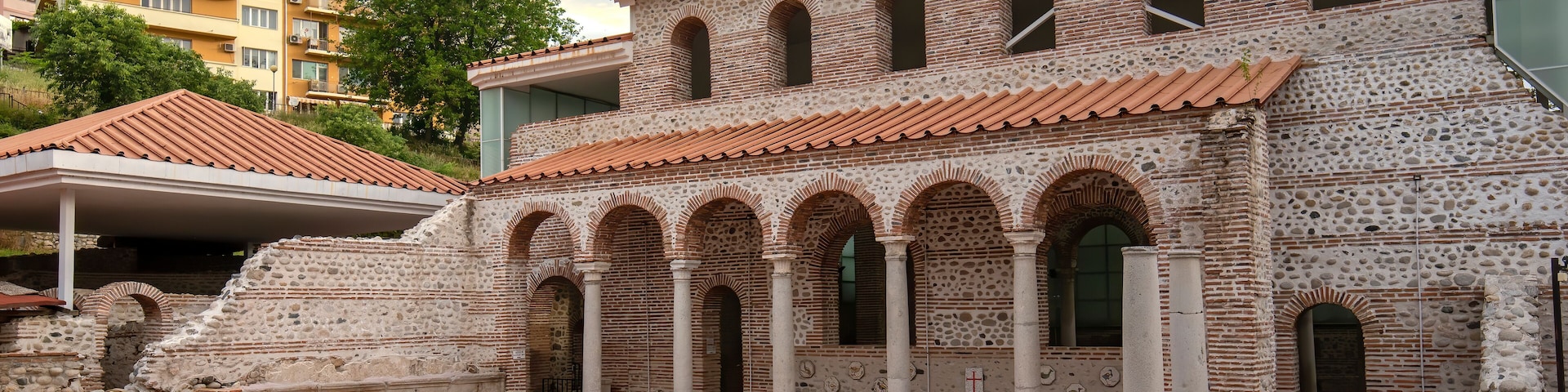 Un antiguo patio con columnas y arcos de piedra, rodeado de edificios modernos.