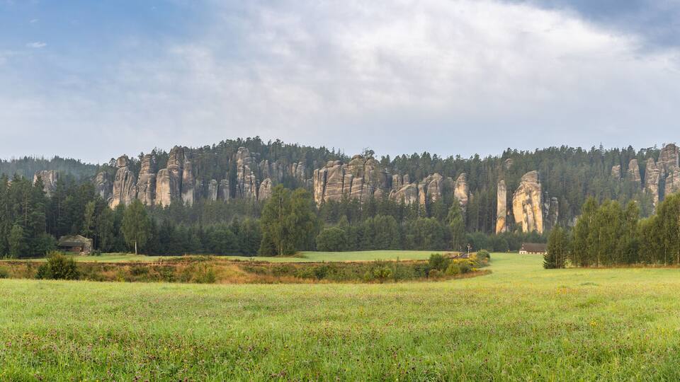 Landscape of Adrspach-Teplice Rocks area, in Hradec Kralove Region in Czech Republic, Europe. Scenic panorama of rock formations, lush forests, and a meadow under a cloudy sky, early morning light.