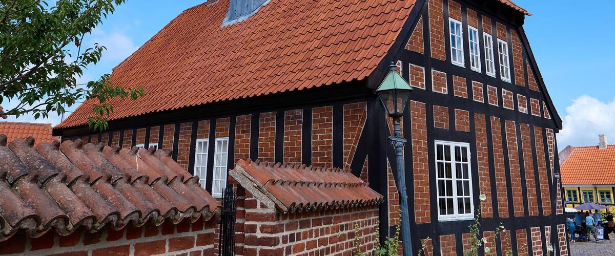 A traditional half-timbered building with a red-tiled roof and a tower with a weather vane.