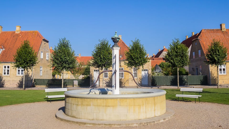 A courtyard with a central fountain, surrounded by traditional buildings with red-tiled roofs.