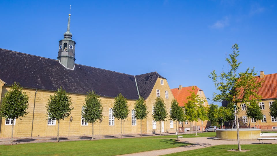 A historic building with a clock tower, surrounded by a well-maintained lawn and trees.
