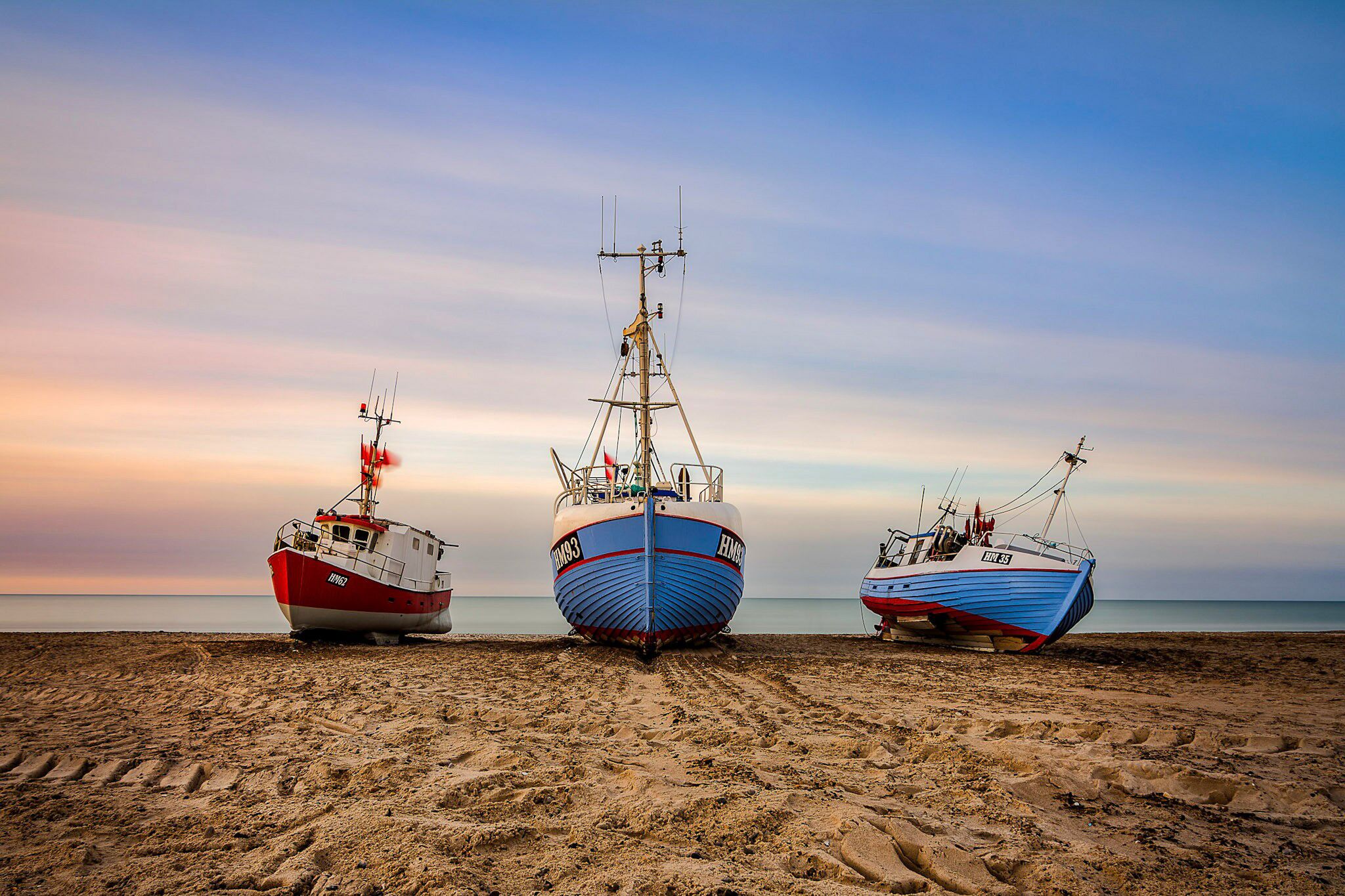 Three fishing boats on a sandy beach with a calm sea in the background.