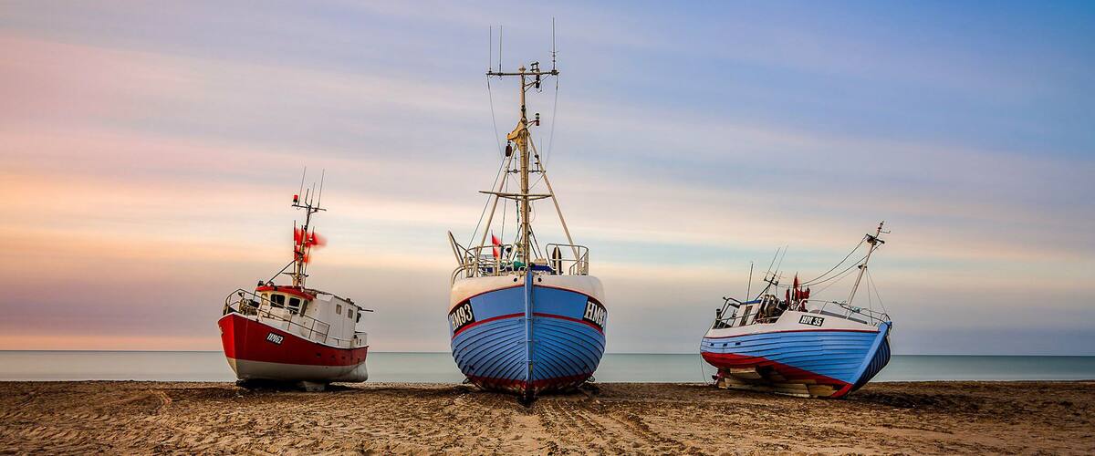 Three fishing boats on a sandy beach with a calm sea in the background.