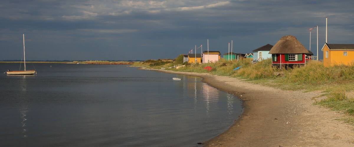 A coastal scene with a sandy beach, a small boat, and colorful houses by the water.