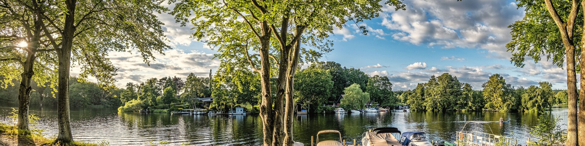 A serene lakeside scene with boats docked, surrounded by lush trees and a clear sky.