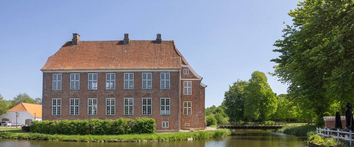 A large brick building with a tiled roof by a calm river.