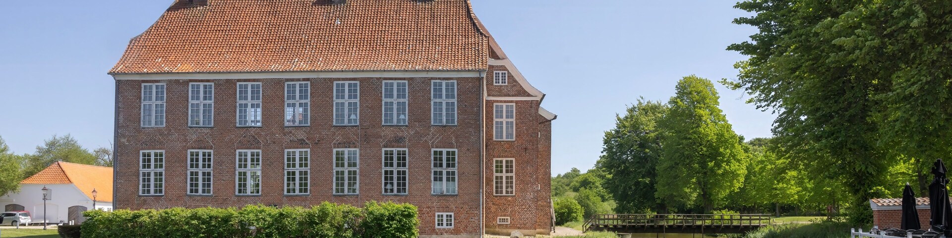 A large brick building with a tiled roof by a calm river.