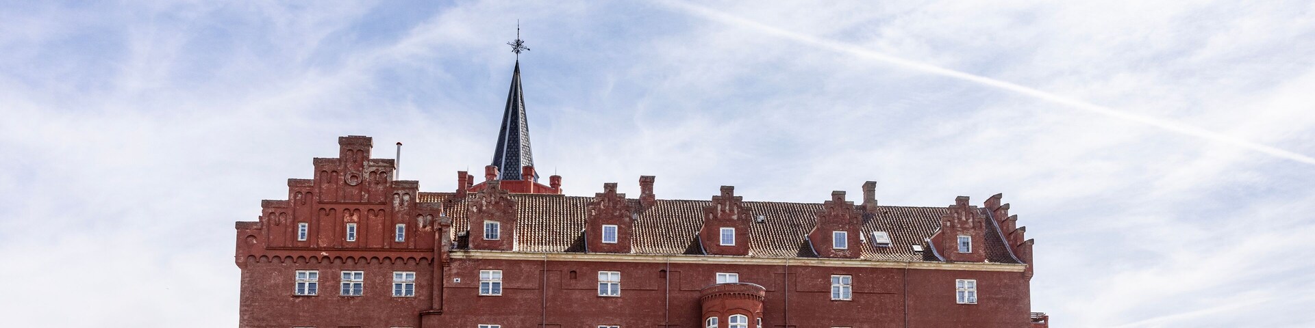 A large red brick castle with a spire, surrounded by green grass and cacti.