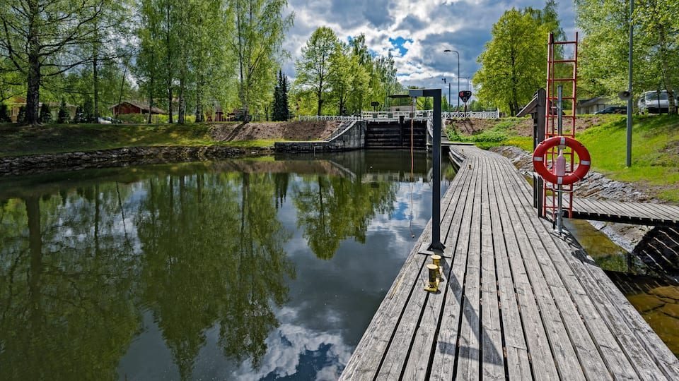 A wooden dock extending over a calm river, surrounded by lush greenery and trees.