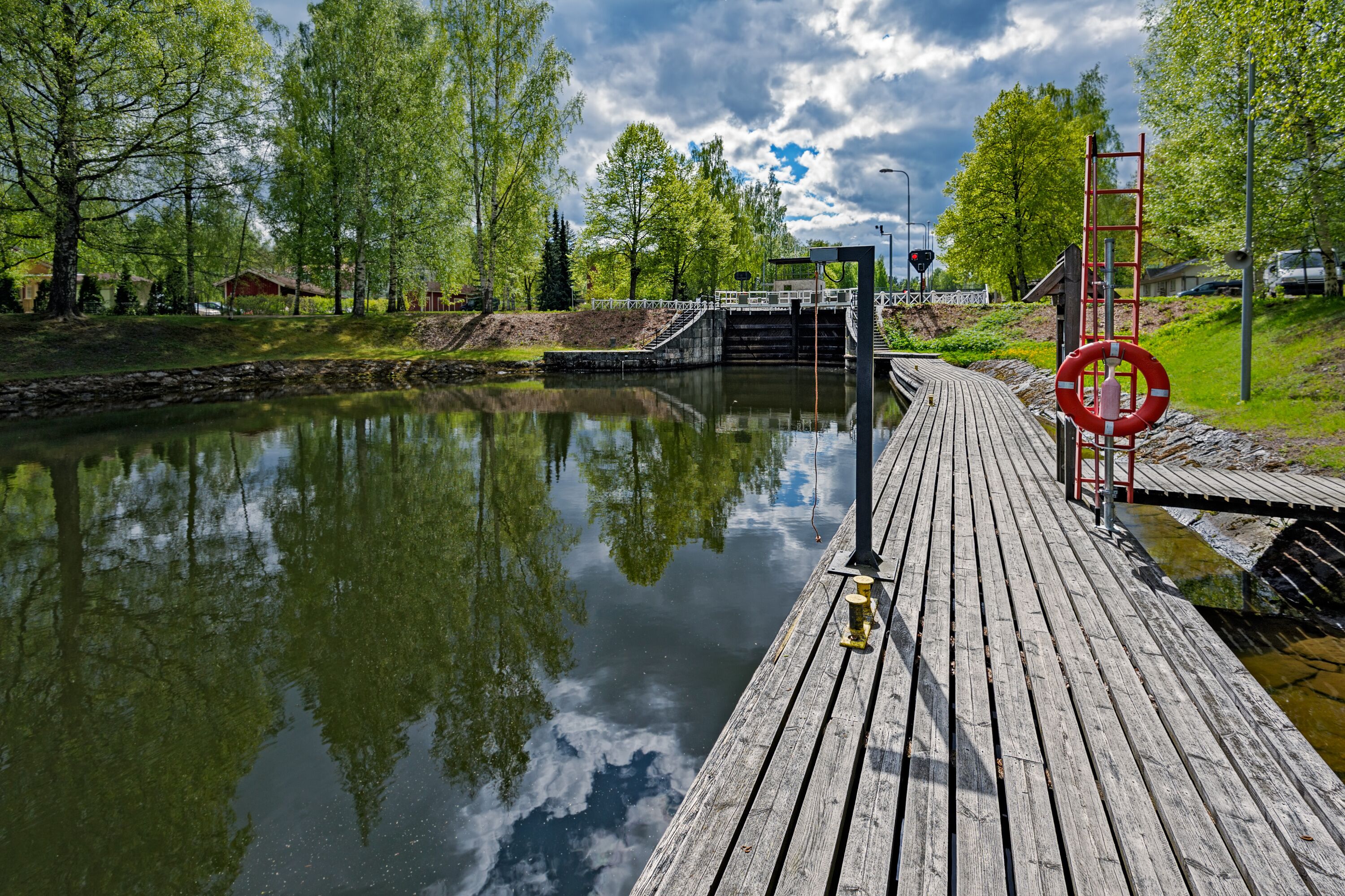 A wooden dock extending over a calm river, surrounded by lush greenery and trees.