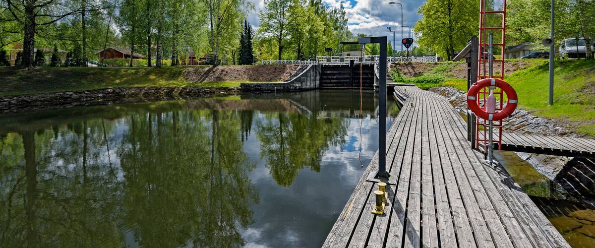 A wooden dock extending over a calm river, surrounded by lush greenery and trees.