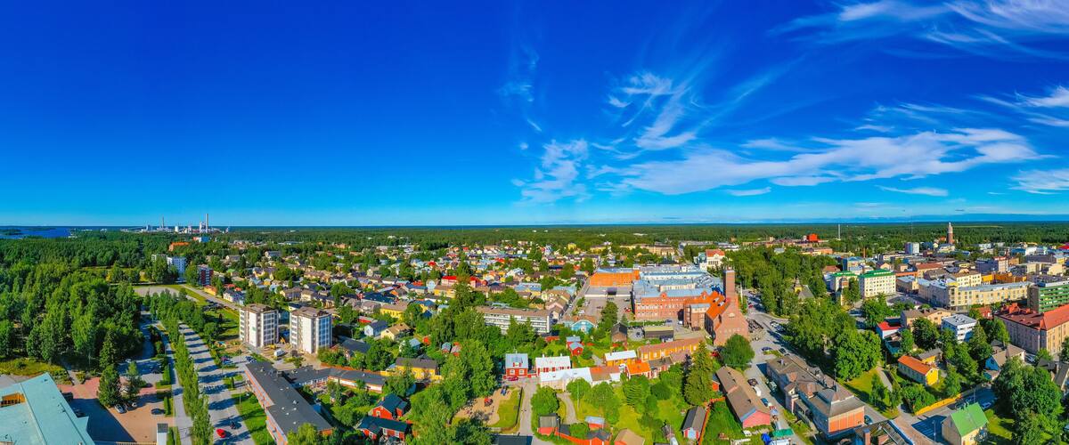 An aerial view of a town with a mix of residential and commercial buildings, surrounded by greenery and a clear blue sky.