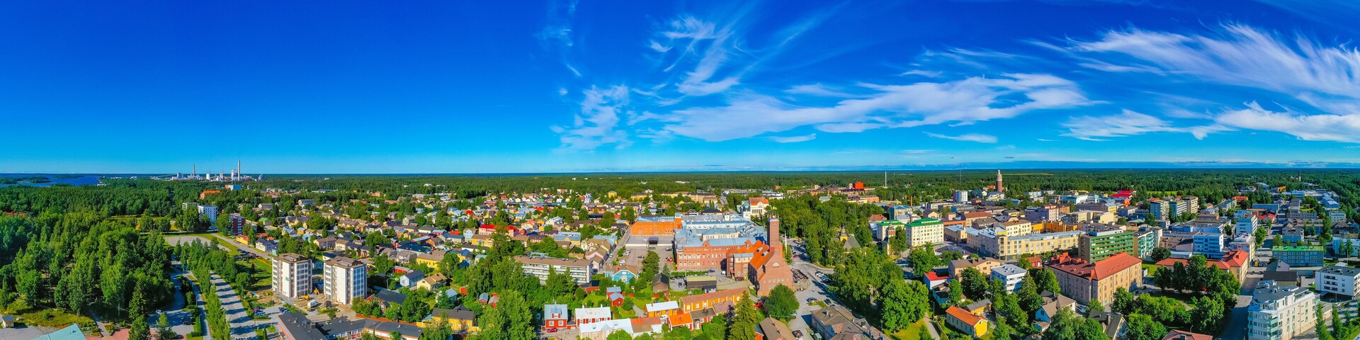 An aerial view of a town with a mix of residential and commercial buildings, surrounded by greenery and a clear blue sky.