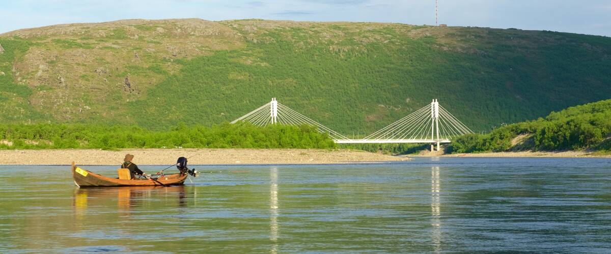 A river with a wooden boat, a bridge, and a hill in the background.